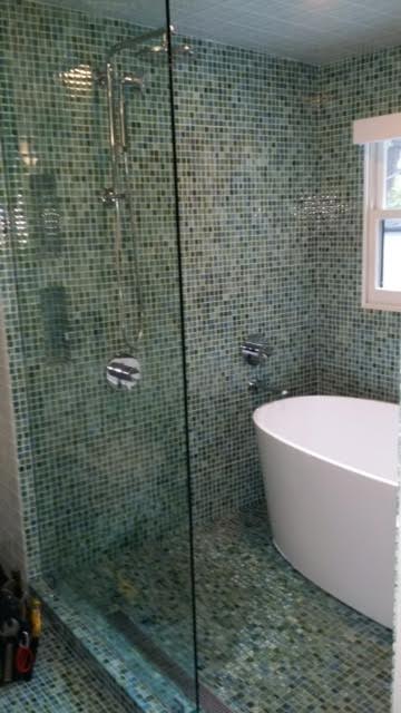 Custom designed oval bathtub in glass and tile shower.